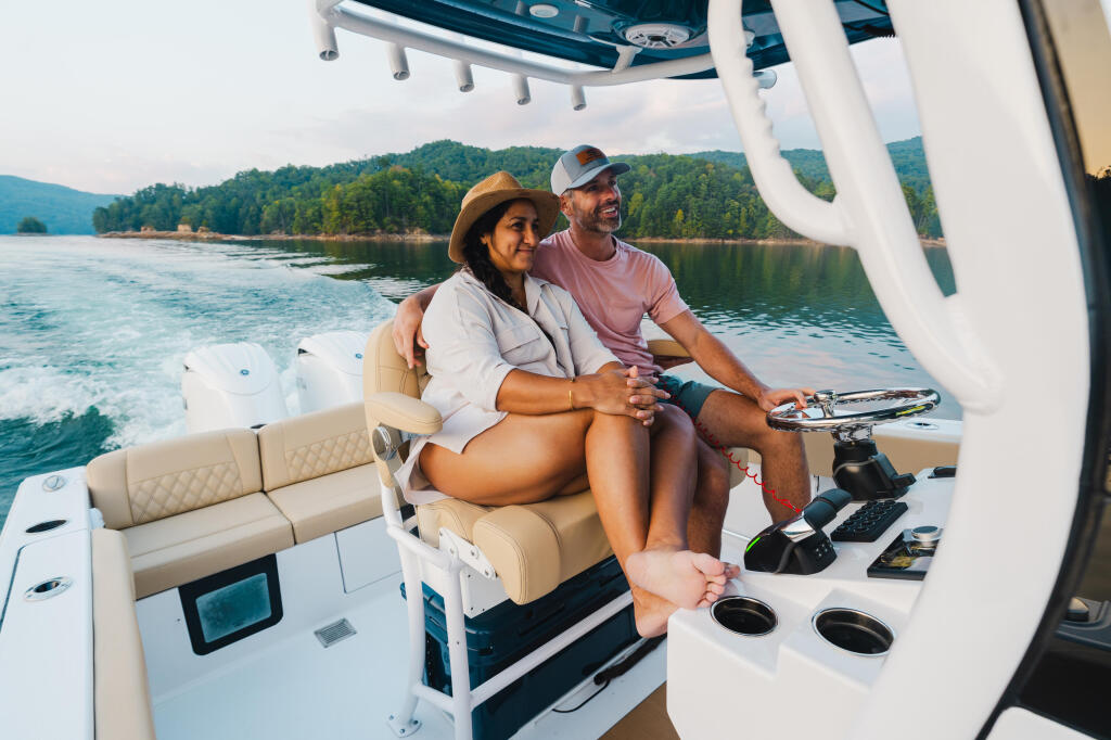 Couple relaxing on boat seating with scenic lake and forested shoreline in background