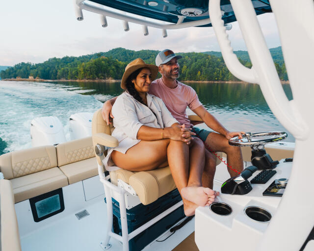 Couple relaxing on boat seating with scenic lake and forested shoreline in background
