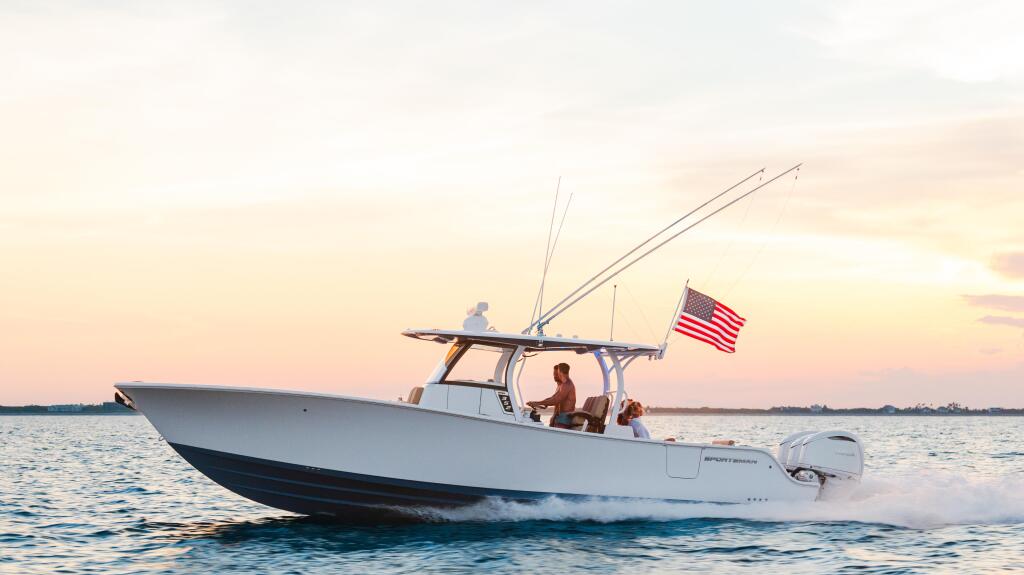 White fishing boat with hard-top cruising through shallow water at sunset with couple aboard and American flag flying