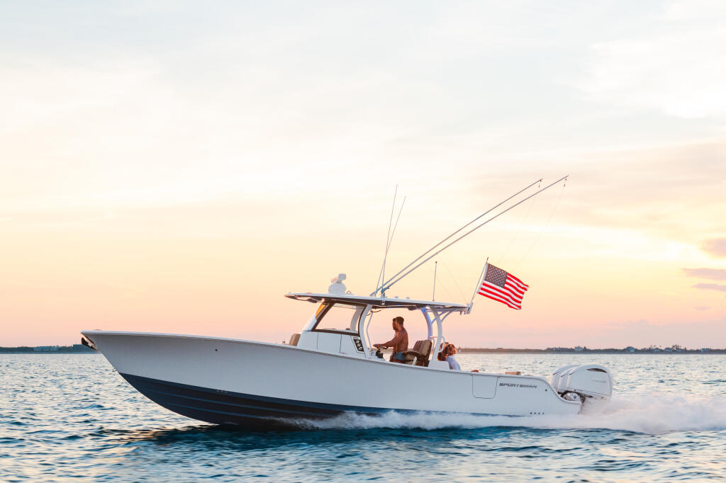 White fishing boat with hard-top cruising through shallow water at sunset with couple aboard and American flag flying