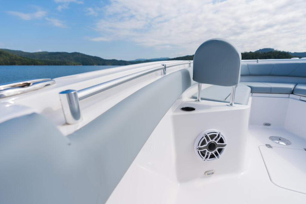 White center console boat with railing and speaker on calm lake with forested mountains in background
