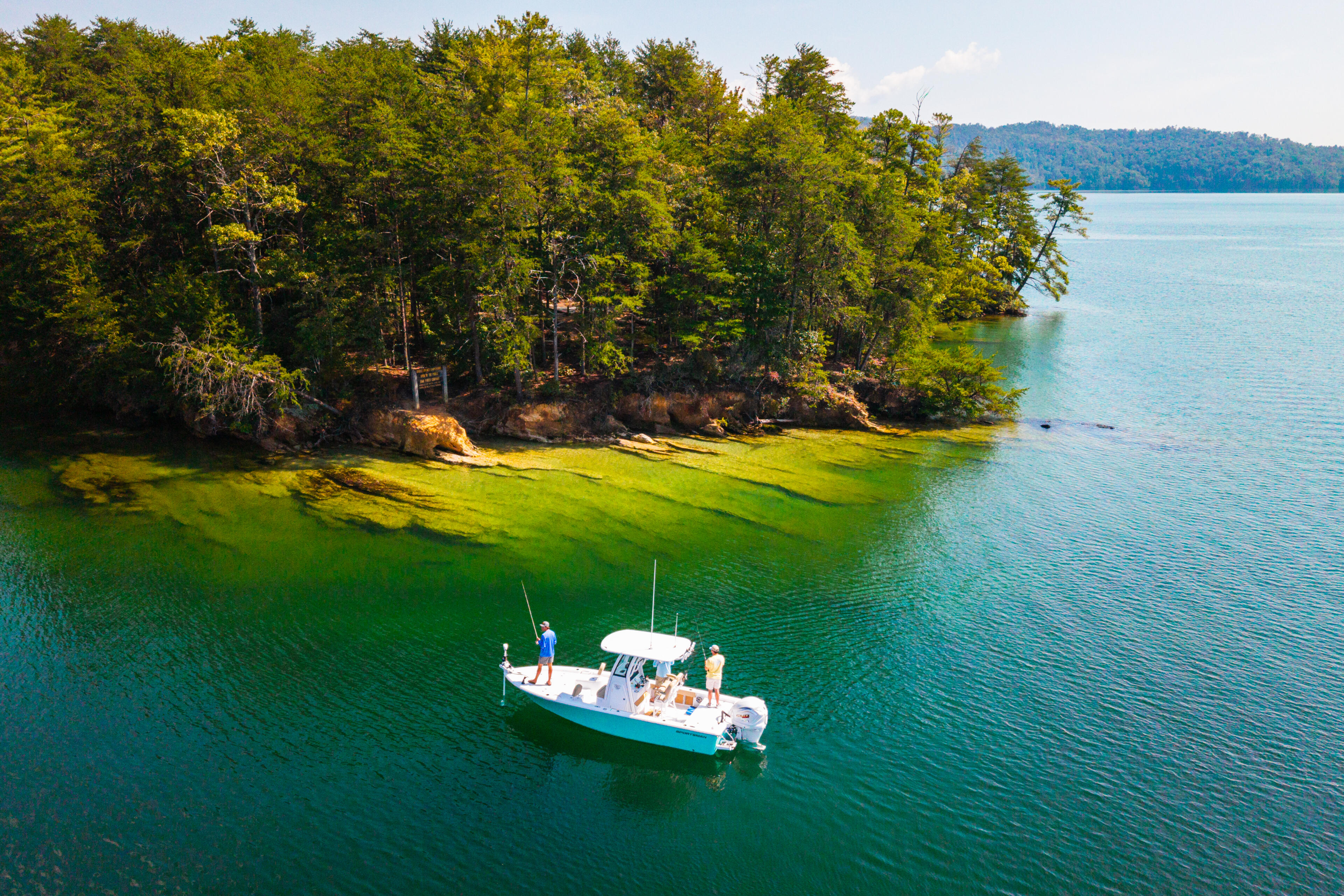 Fishing boat anchored in turquoise water near forested shoreline with rocky outcrops