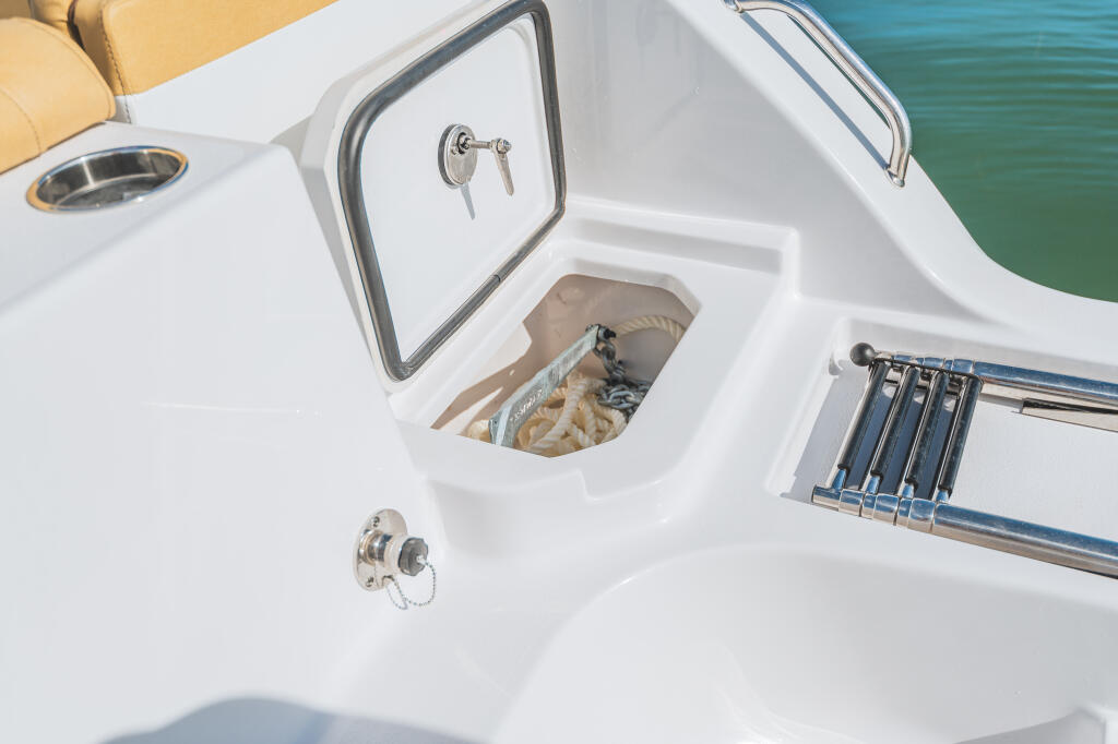 Overhead view of boat's stern showing open storage locker with rope and anchor setup near turquoise water