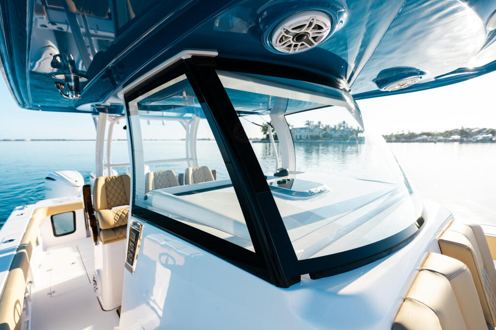Hard-top cabin interior with quilted tan seating, windshield view of calm water and distant shoreline