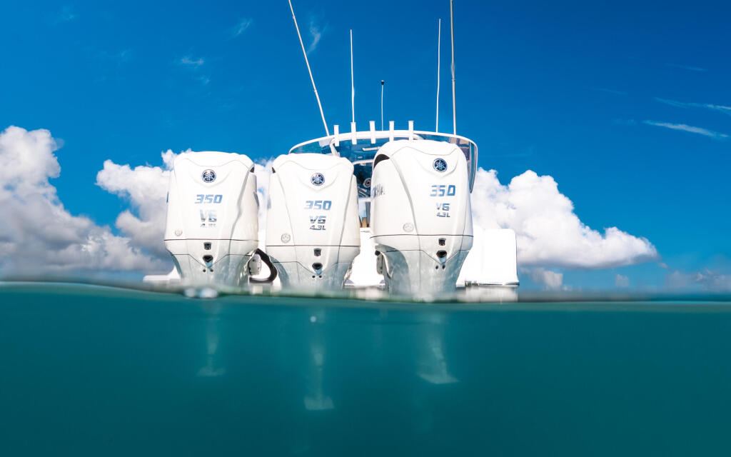 Triple-engine center console boat anchored in shallow turquoise water with split aerial and underwater view