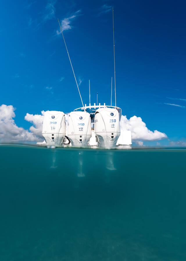 Triple-engine center console boat anchored in shallow turquoise water with split aerial and underwater view