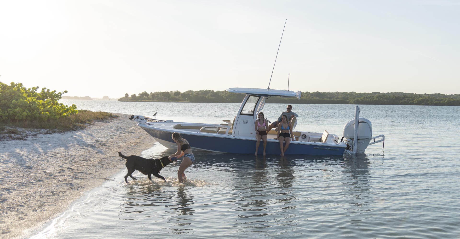 Family with dog wading to center console boat anchored in shallow sandy beach waters