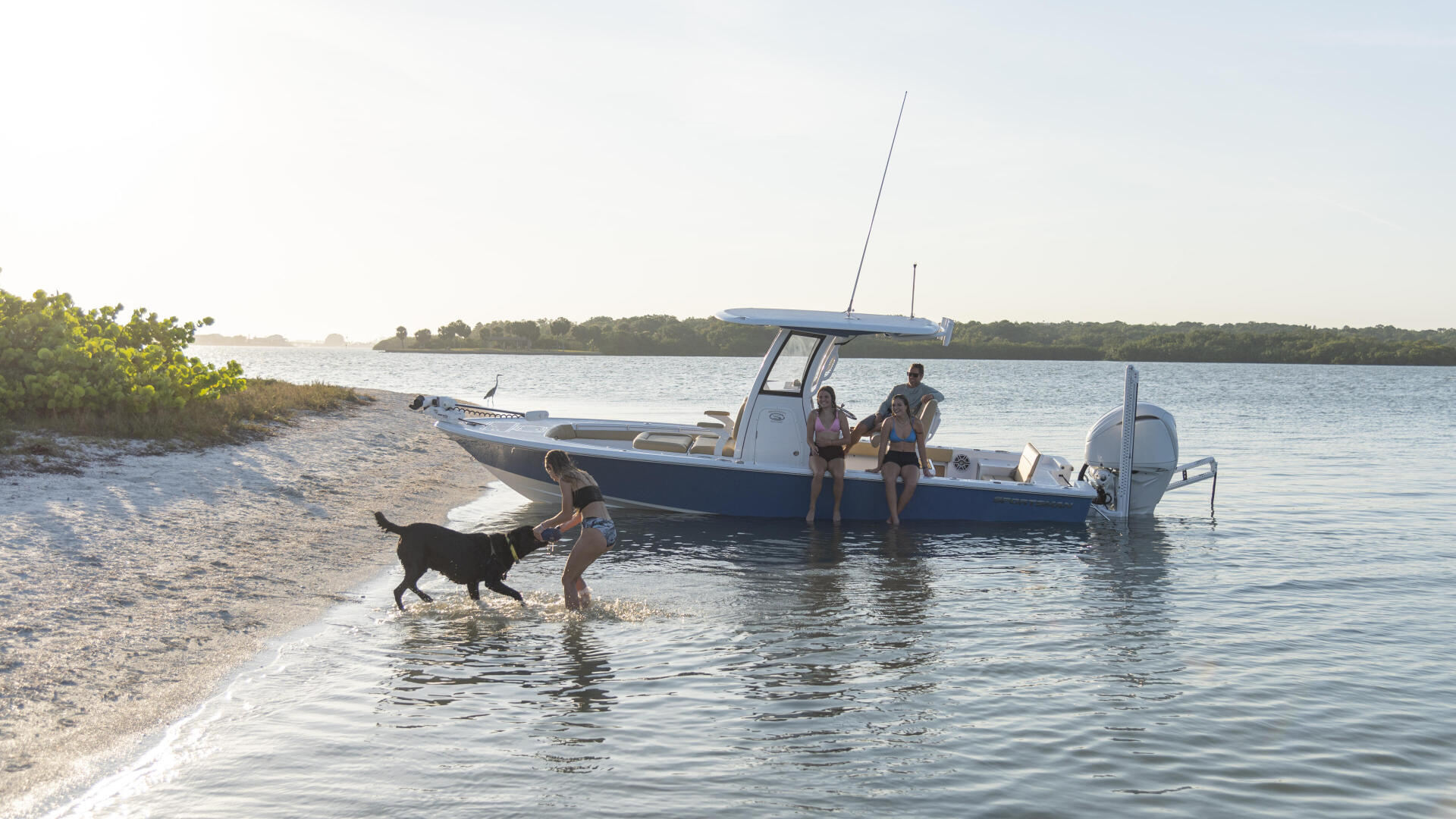Family with dog wading to center console boat anchored in shallow sandy beach waters