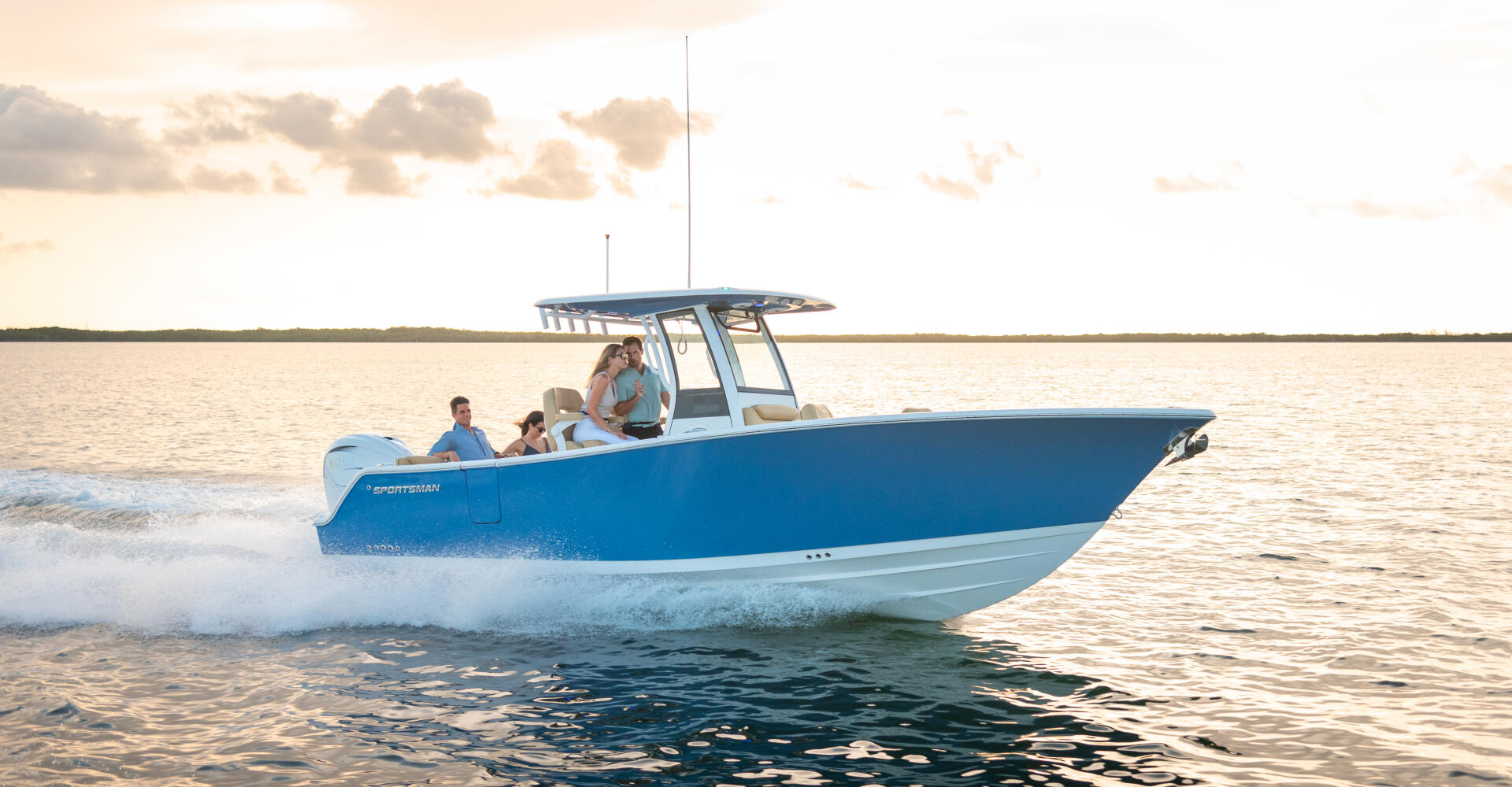 Blue and white center console boat with family aboard cruising through shallow coastal waters near beach at sunset