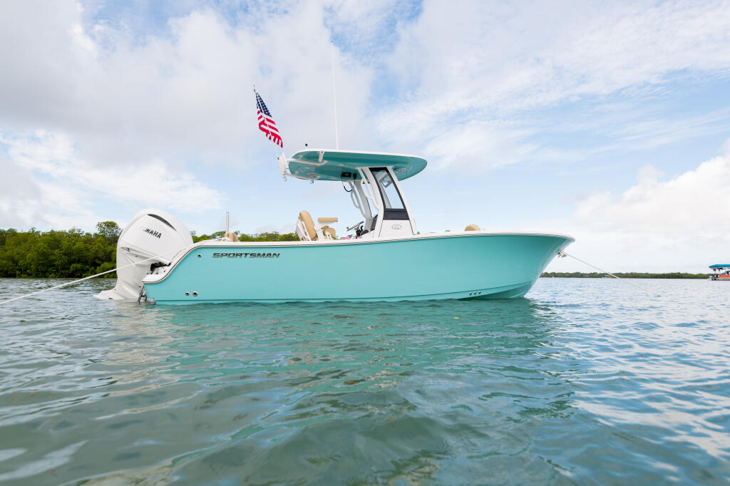 Turquoise Sportsman center console boat anchored in shallow water with American flag and hard-top canopy