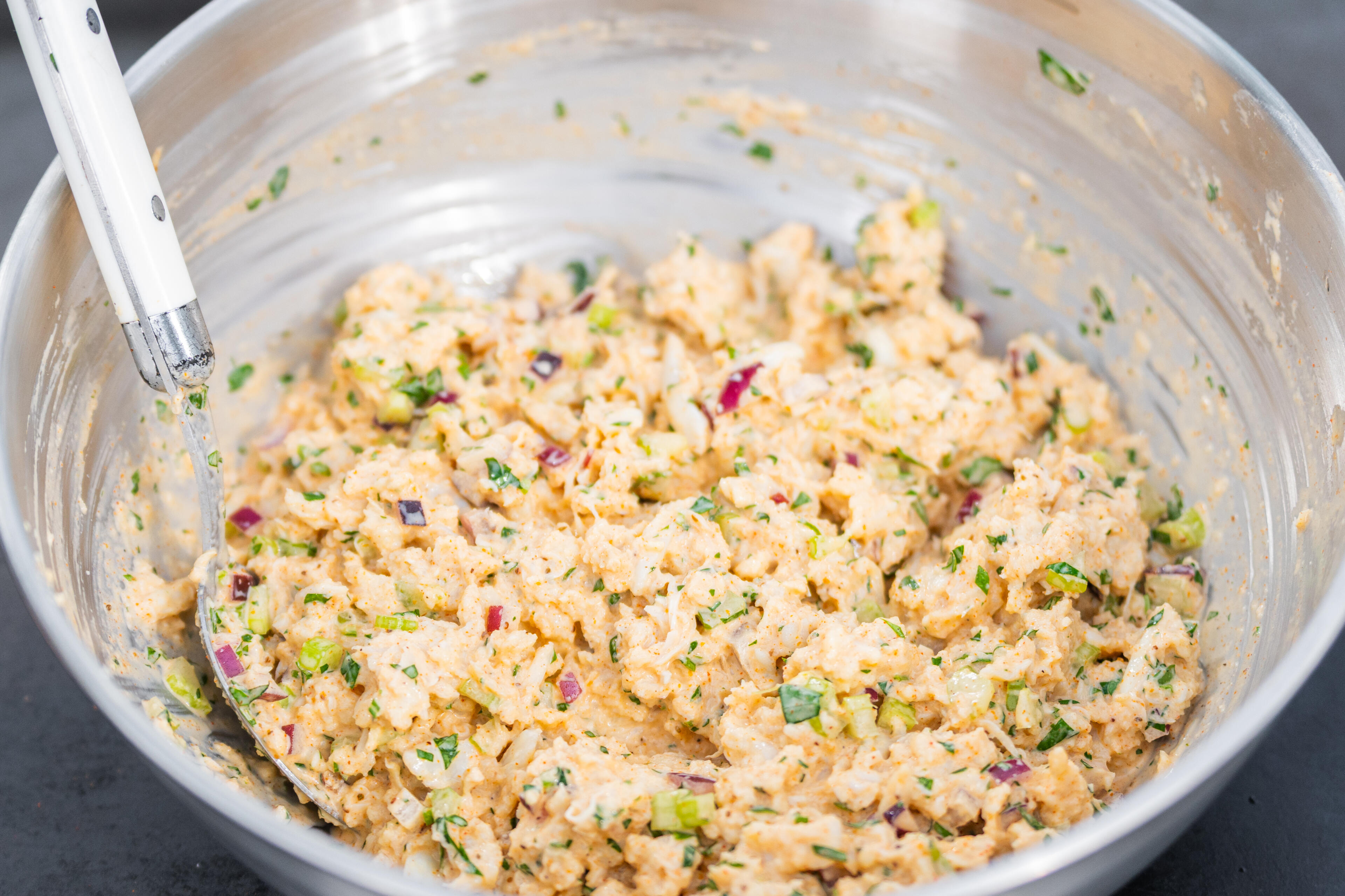 Crab mixture with green onions and red peppers in a white mixing bowl with a spoon