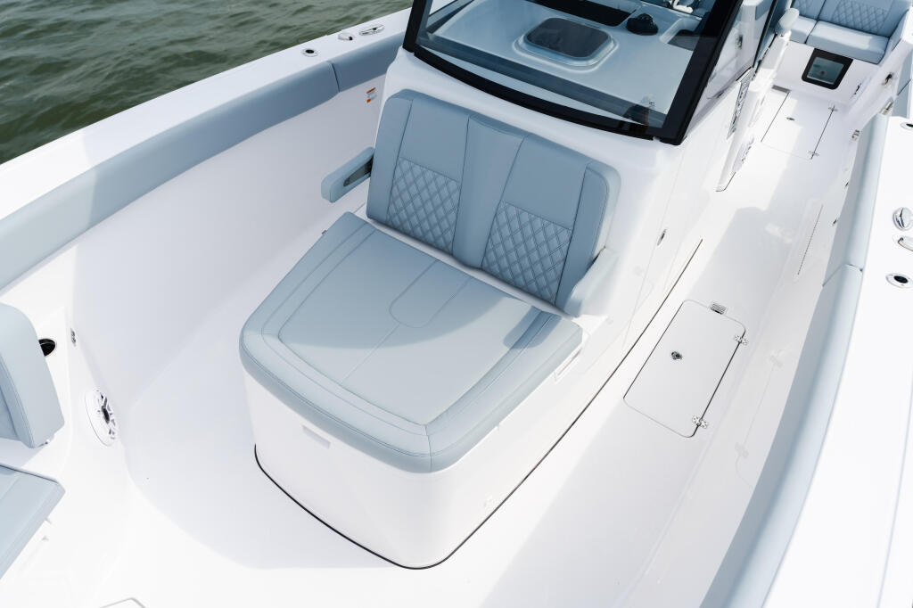 Open-bow seating area with gray quilted upholstery and white gel-coat deck, windshield visible at helm