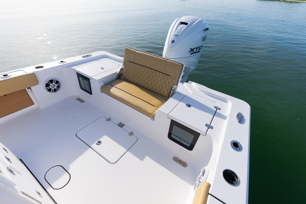 White center console boat deck with tan upholstered fold-up bench seat, electronics display, and XTI outboard engine