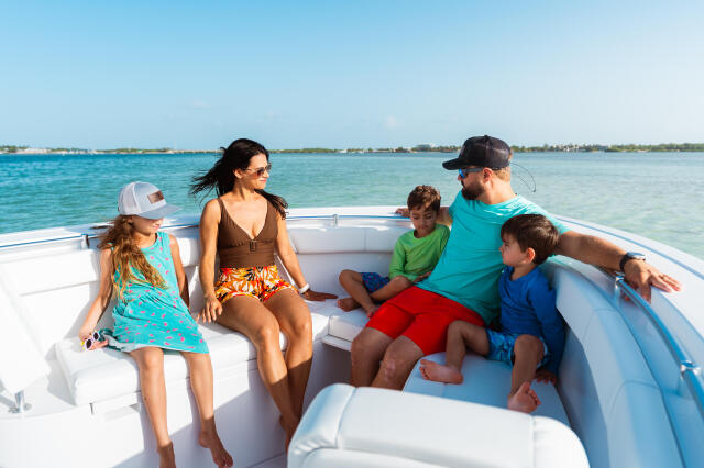 Family of five enjoying a sunny day on a boat in turquoise shallow water near a sandbar