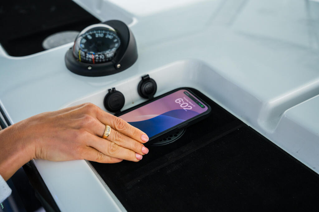 Hand operating smartphone GPS display mounted on boat helm near compass and control buttons