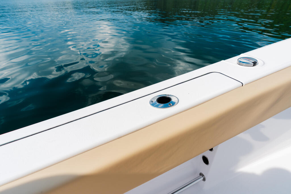 Boat gunwale with white trim and blue water alongside, showing flush-mount hardware details