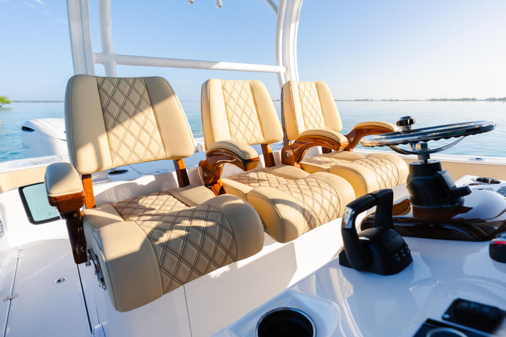 Cream and tan quilted helm seating with wooden armrests on a center console boat with calm blue water visible beyond