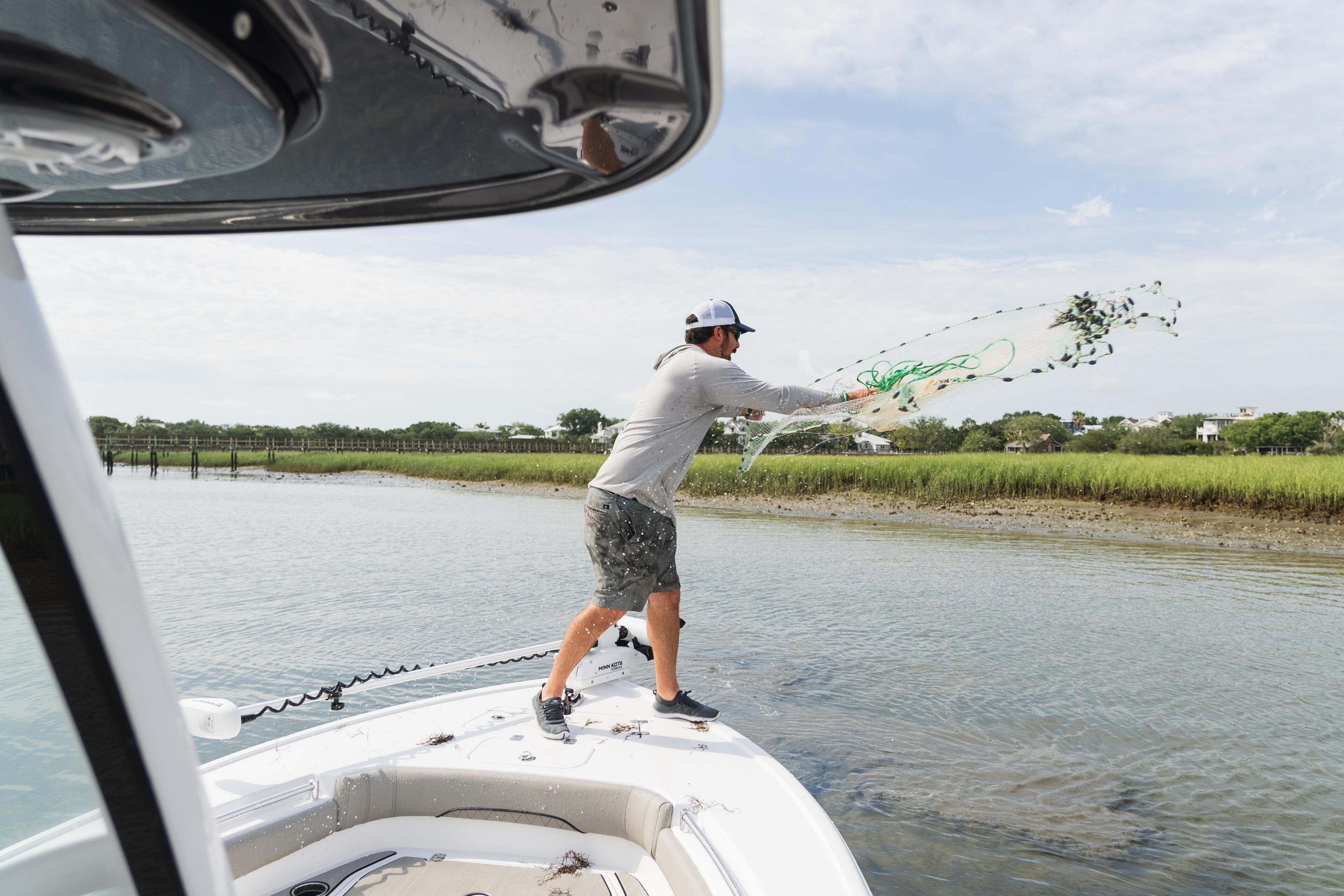 Angler casting a net from the bow of a boat in shallow coastal waters