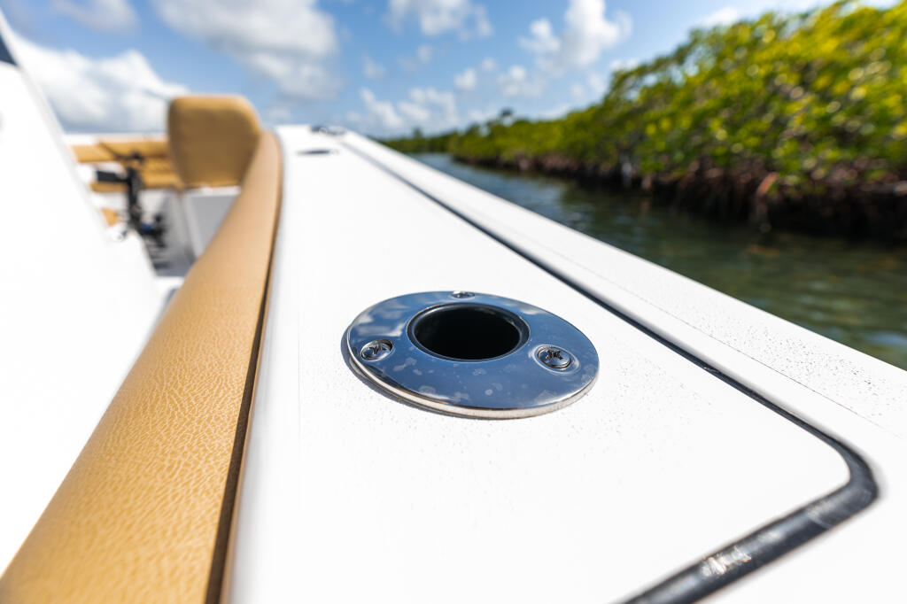 Flush-mount rod holder detail on white boat gunwale with tan trim and mangrove shoreline in background