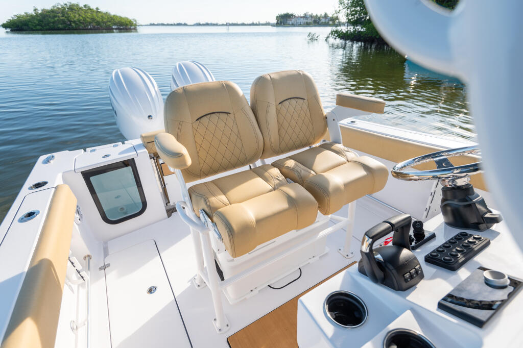 Center console boat with tan quilted seating, helm station with electronics, and dual outboard engines docked in calm coastal waters