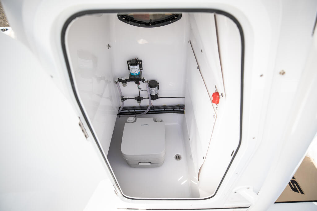 Overhead view of boat head showing portable toilet, water system pump, and plumbing connections installed in compact cabin space