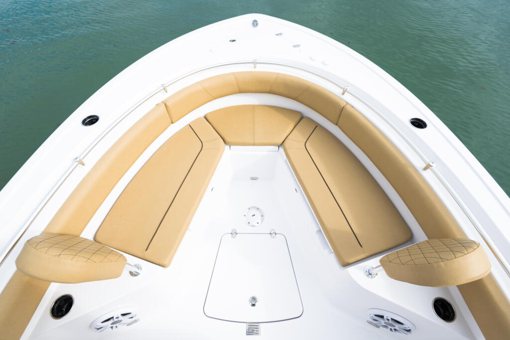 Overhead view of boat's bow seating with tan cushioned seats and white gel coat hull over turquoise water