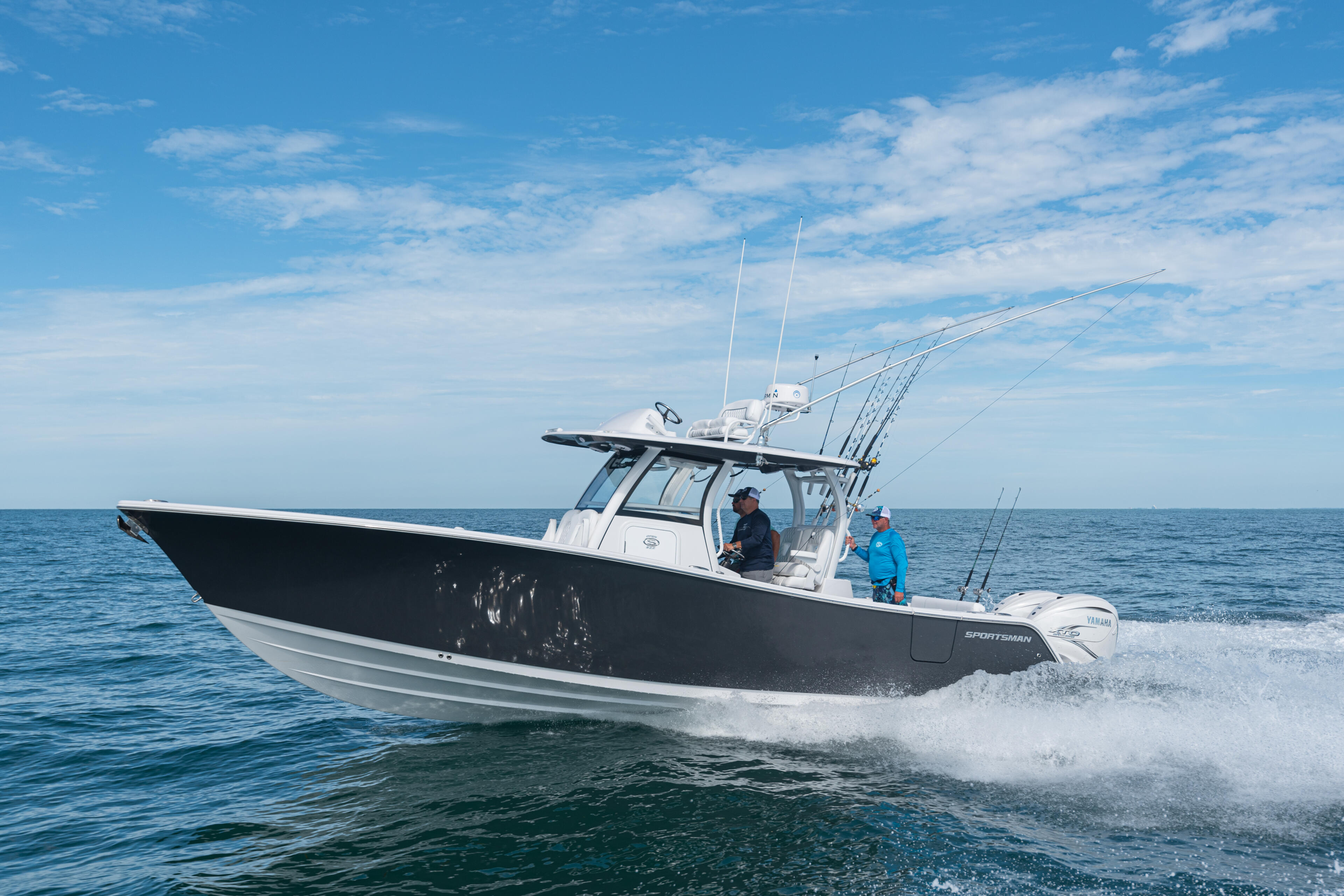 Black and white fishing boat running through shallow beach waters with two people aboard on a clear blue day