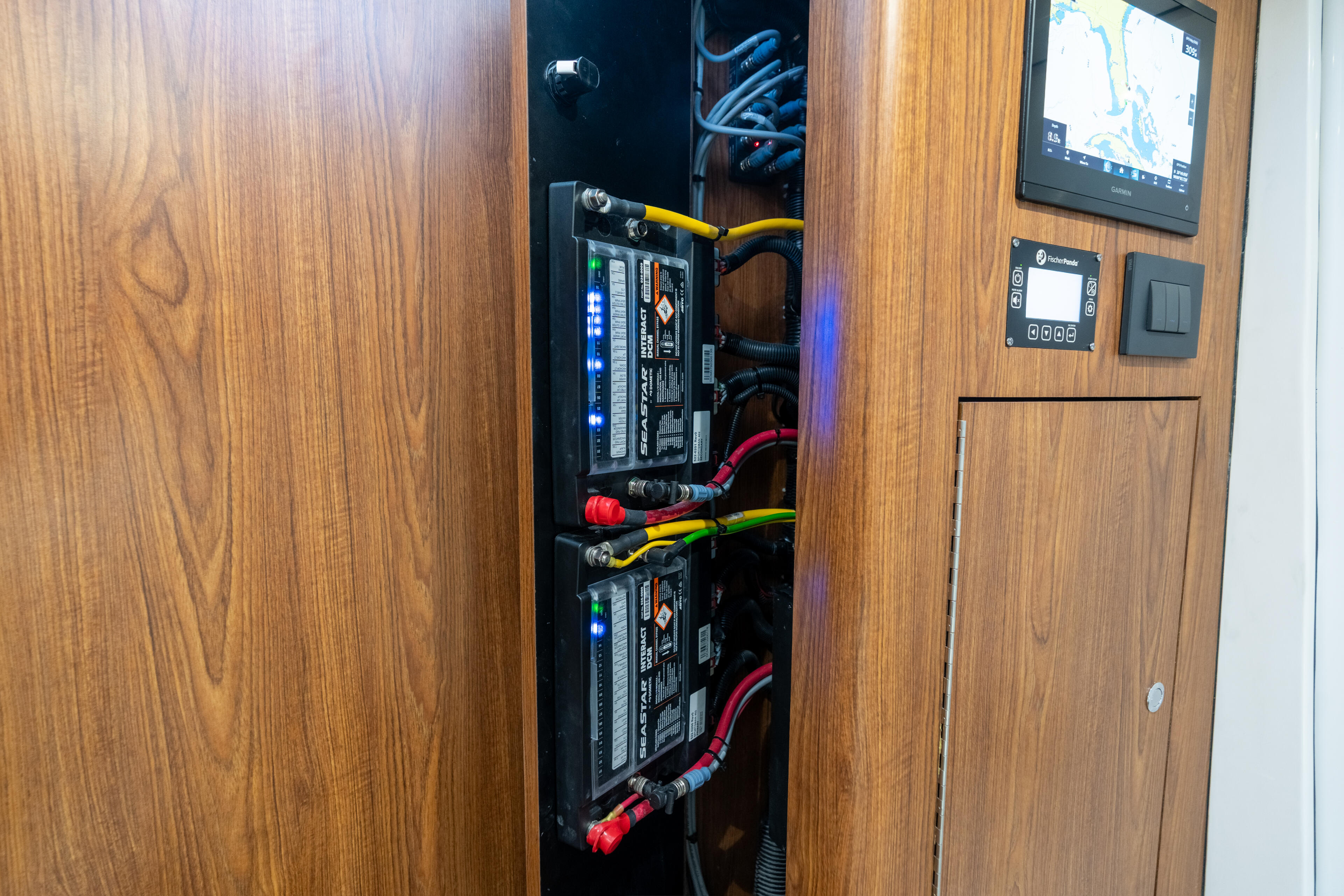 Boat cabin electrical panel with dual battery systems, blue LED indicators, and color-coded power cables mounted in wood-trimmed interior