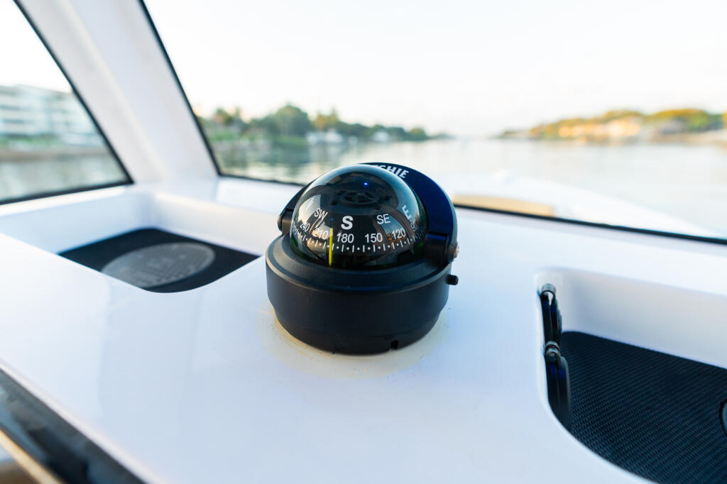 Compass mounted on the helm of a white center console boat with waterfront in background