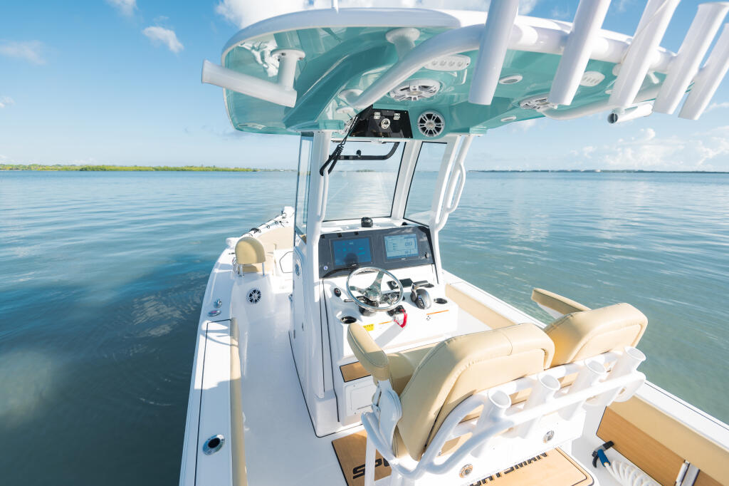 Console helm area of bay boat with tan seating, touchscreen electronics, and teal hard-top canopy under clear sky