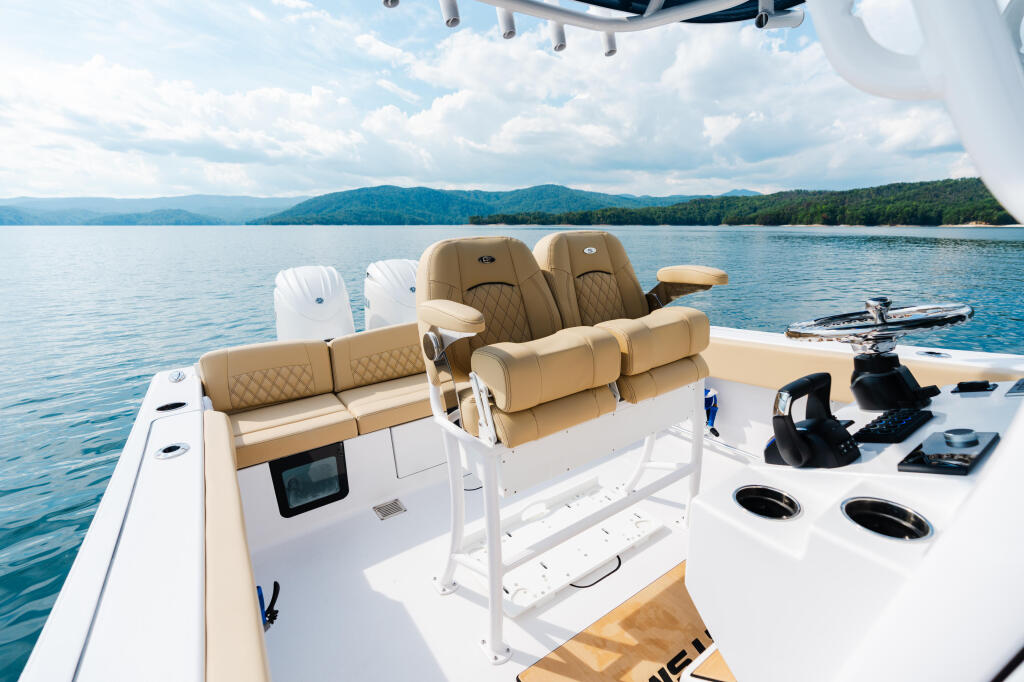 Tan and white boat helm with comfortable seating, electronics, and mountain lake backdrop