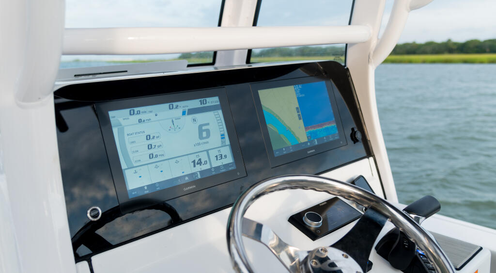 Helm station with dual touchscreen displays showing navigation and depth data, steering wheel, and water view ahead