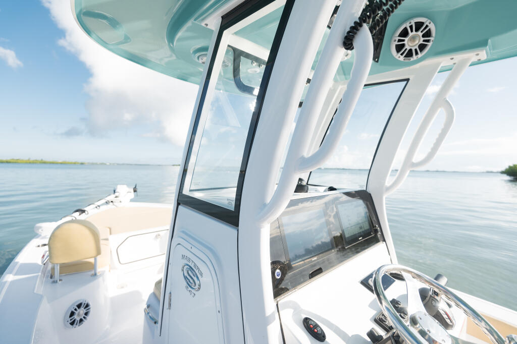 Hard-top boat cabin with steering wheel, windshield, and spacious seating on calm blue water