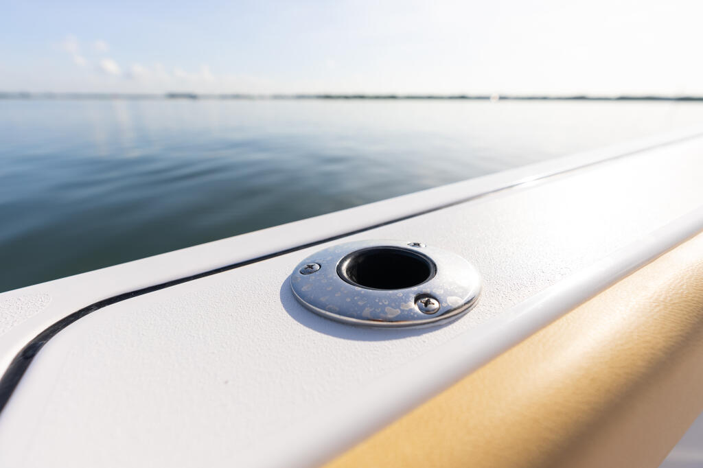 Close-up of a flush-mount gunwale rod holder on a boat's white railing overlooking calm water
