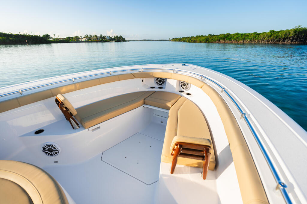 Boat's bow seating area with tan cushions overlooking calm blue water and mangrove shoreline
