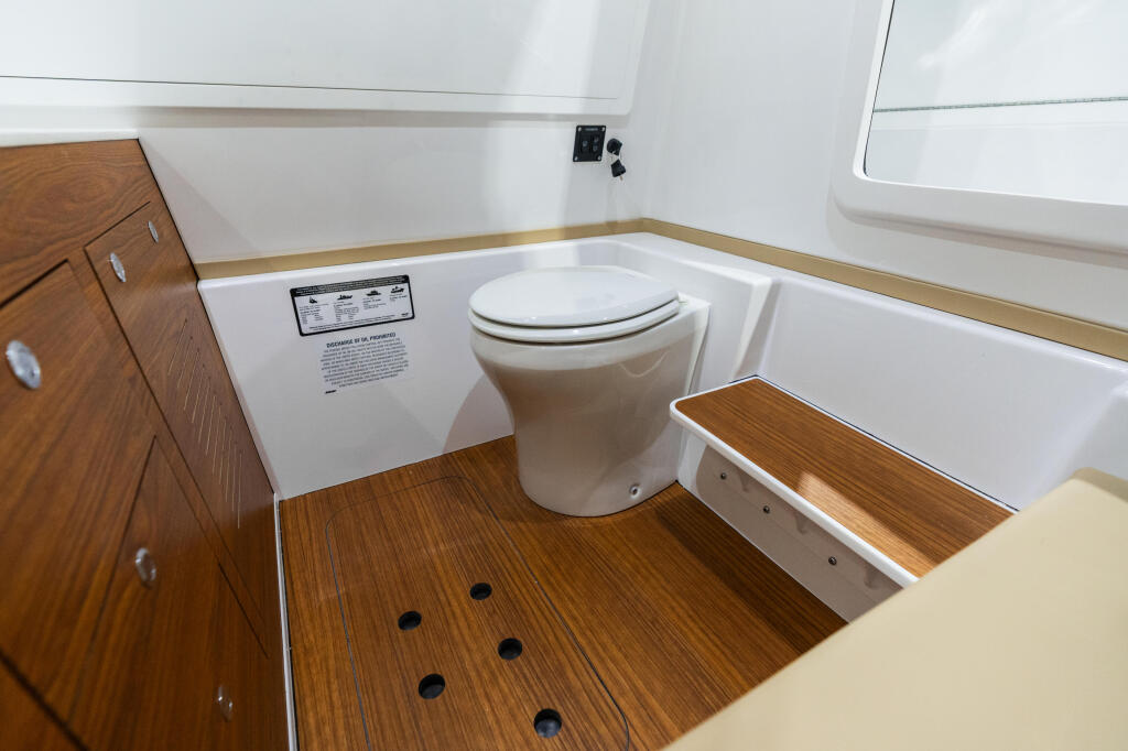 Modern boat cabin head with white porcelain toilet, teak cabinetry, and wood-accented flooring