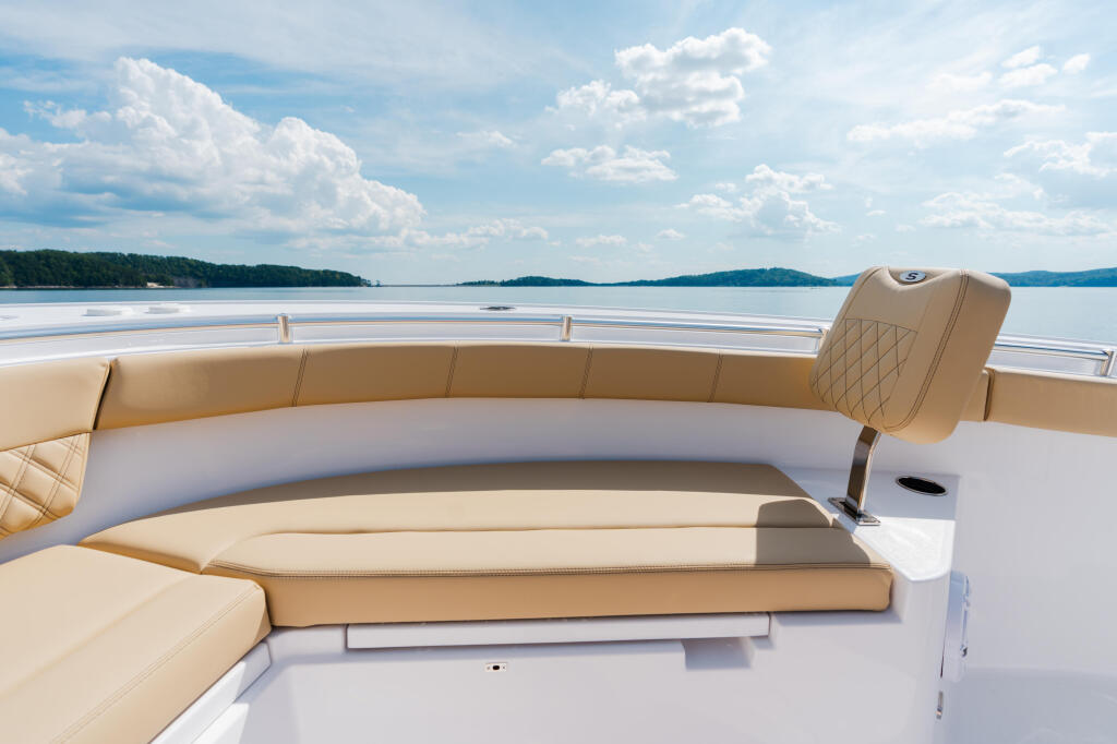 Spacious helm seating area with tan upholstery overlooking calm lake and forested shoreline