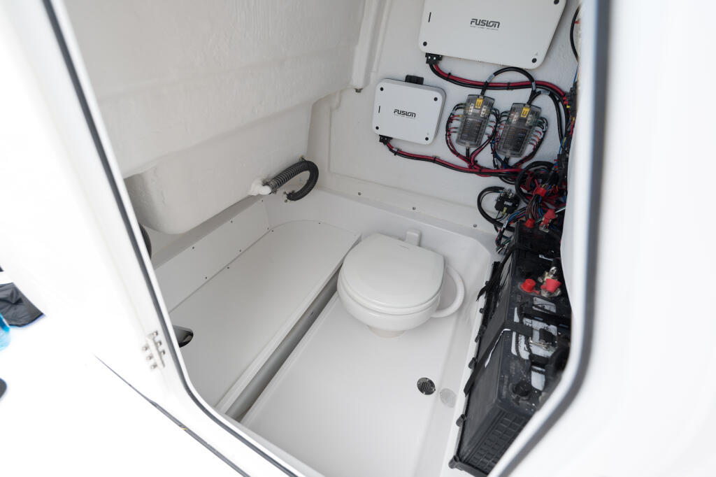 Compact enclosed boat head with white toilet, Fusion audio equipment, and organized electrical wiring on starboard wall