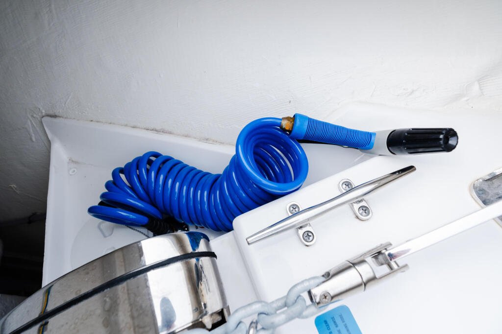 Coiled blue hose and marine hardware mounted on white boat deck with stainless steel cleat and fittings