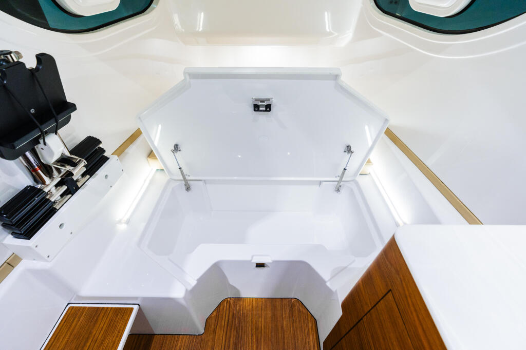 Overhead view of boat cabin showing open hatch, teak flooring, white gelcoat interior, and equipment storage