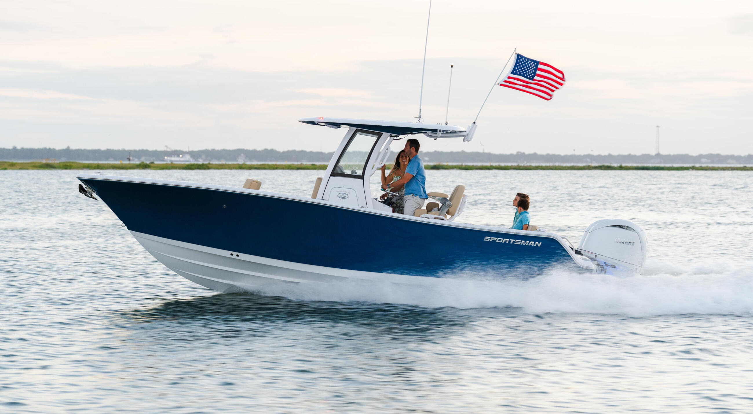 Sportsman boat running through shallow coastal waters with family aboard and American flag flying