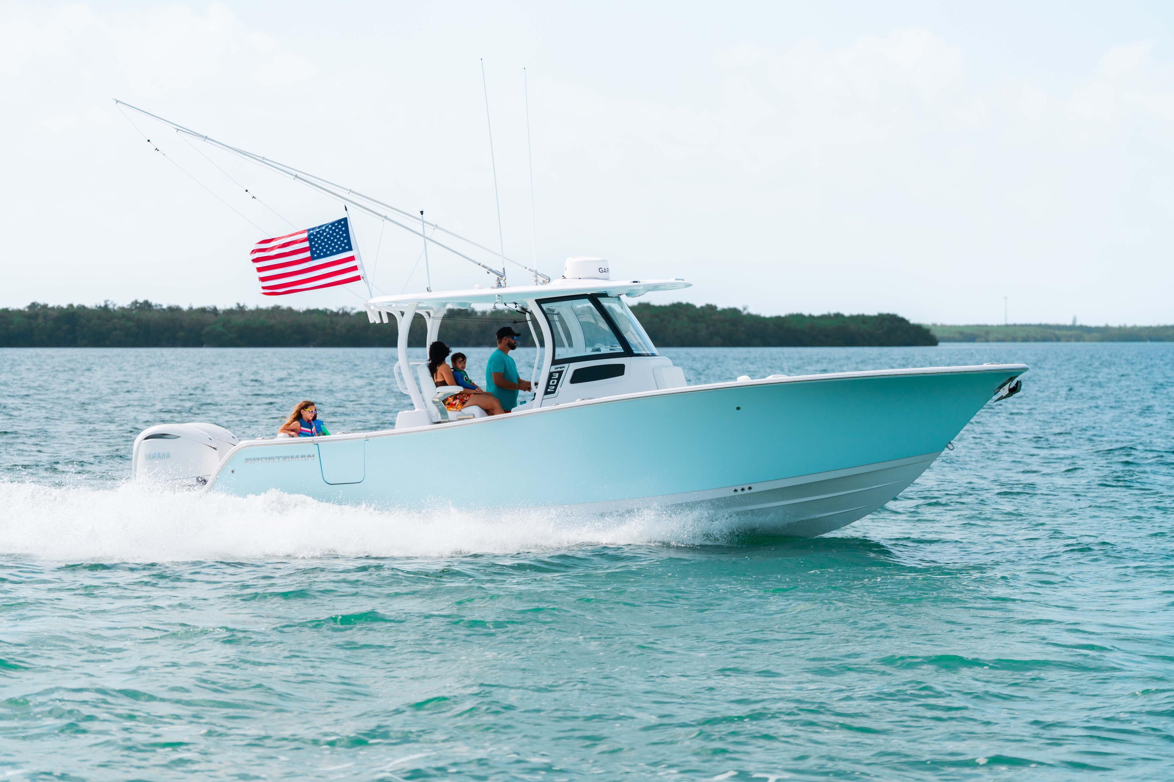 Turquoise and white center console boat running through shallow water with American flag, family aboard enjoying the sandbar