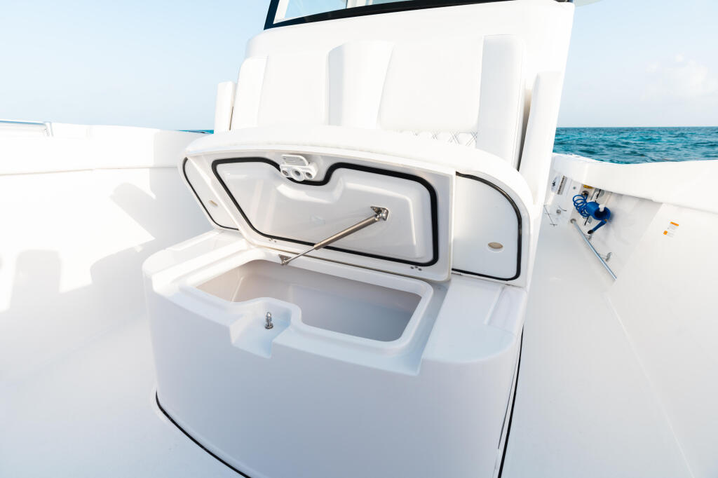 Open livewell with black lid and stainless hardware on white boat deck overlooking calm blue water