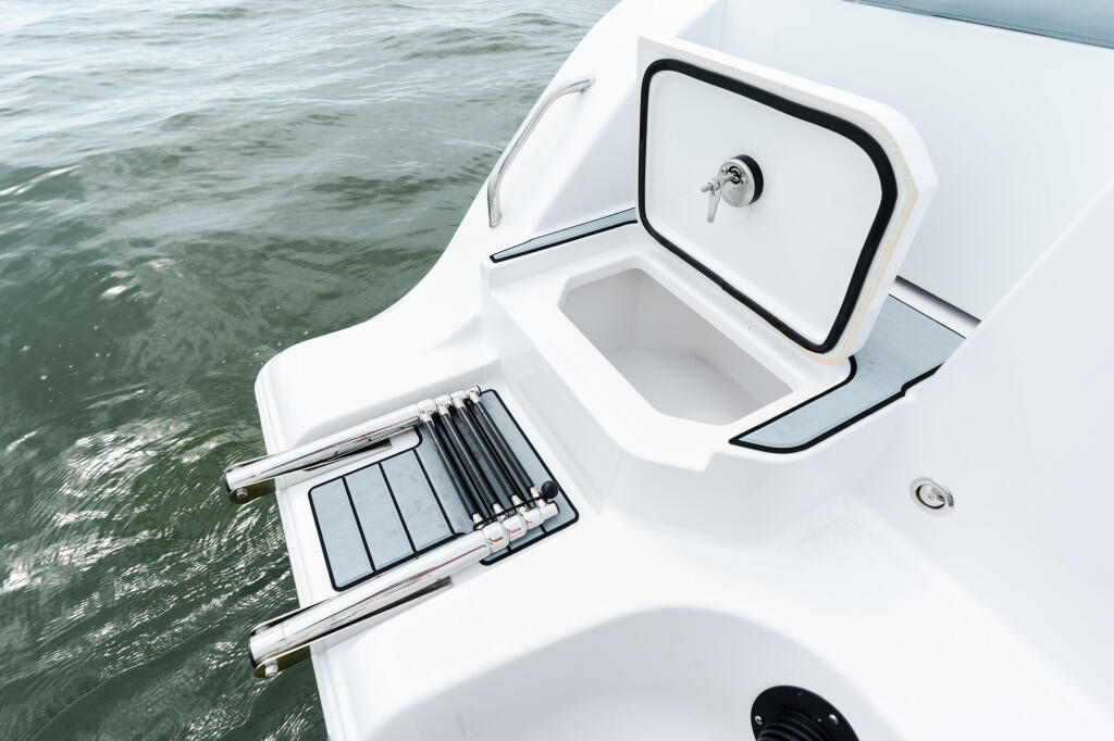 Open livewell and cabin door on white boat hull alongside calm green water