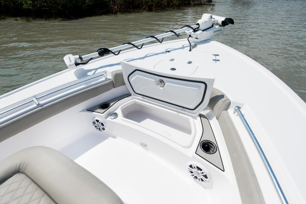 Boat's forward deck with open storage compartment, GPS unit mounted on rail, and mangrove shoreline visible beyond