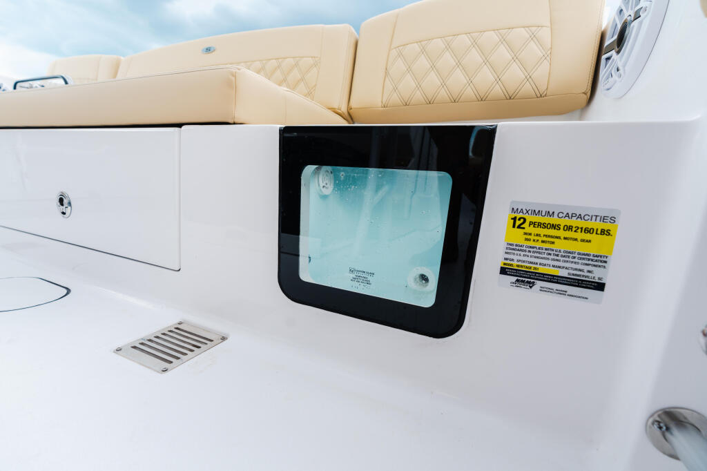 Cream-colored boat seating with quilted cushions, white cabin storage, window, and capacity placard
