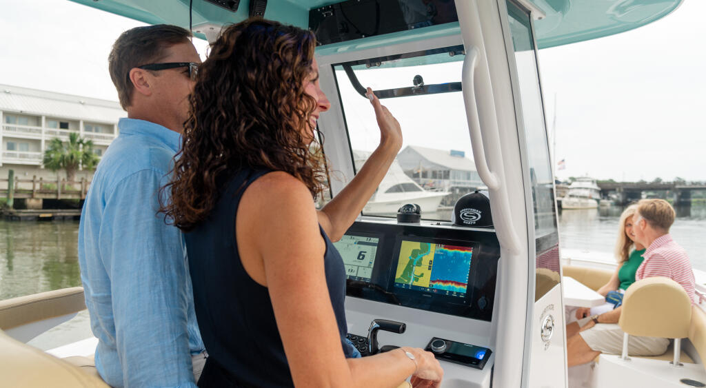 Couple at the helm with electronics display and family aboard a center console boat in a marina