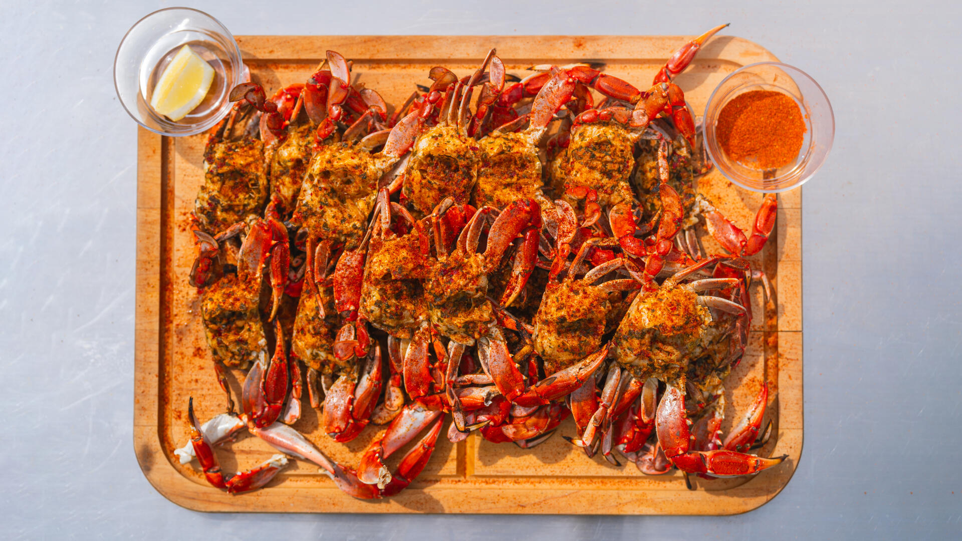 Overhead view of chargrilled crabs seasoned with spices on wooden board with lemon and sauce