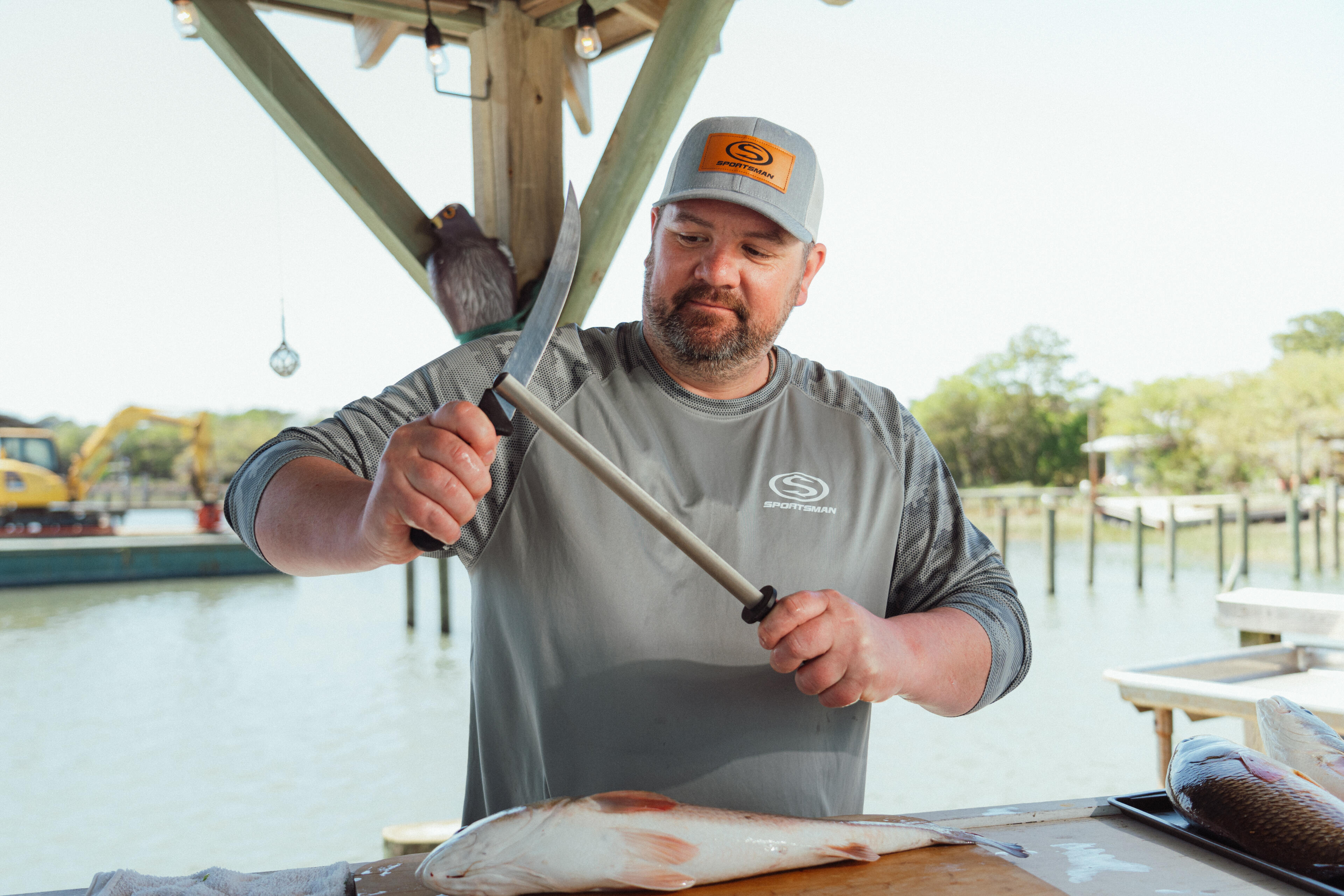 Man in branded cap preparing a fresh redfish at a marina dock