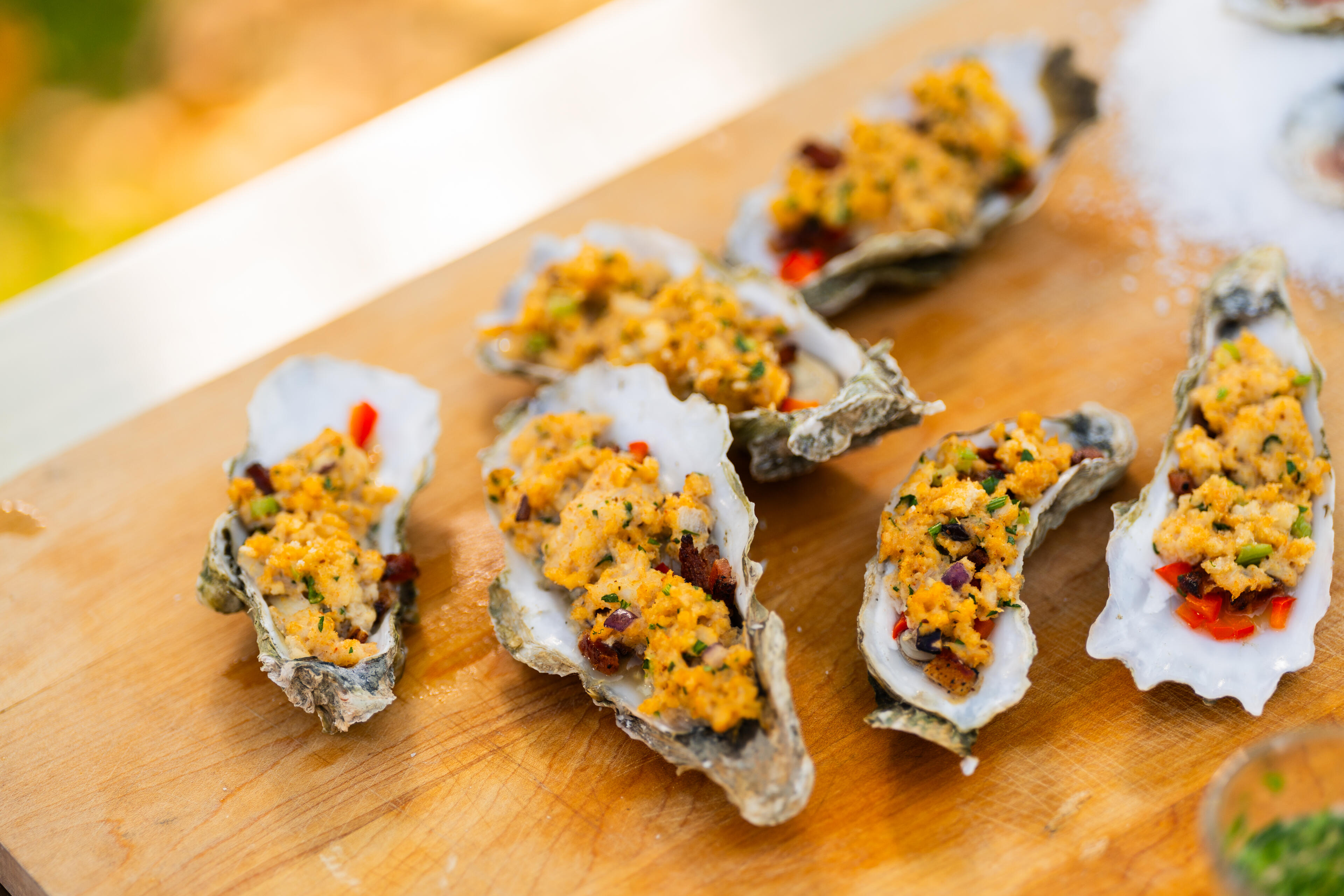 Grilled oysters topped with golden breadcrumb mixture and red peppers arranged on a wooden board